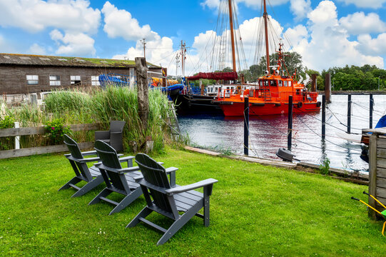 Four chairs on a lawn beside the harbor of Arnis with traditional ships, workboat, reeds and summer sky.