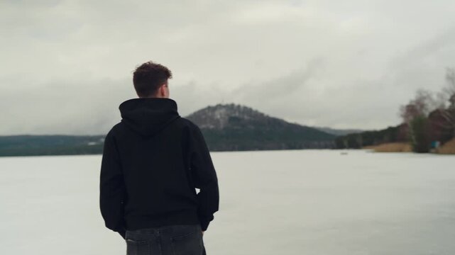 Back view of man standing near Macha Lake looking at snowy hill. Winter travel and solitude concept.