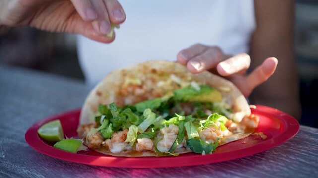 A senior woman smiles as she squeezes lime on fish and shrimp tacos at a taco stand in Baja California.
