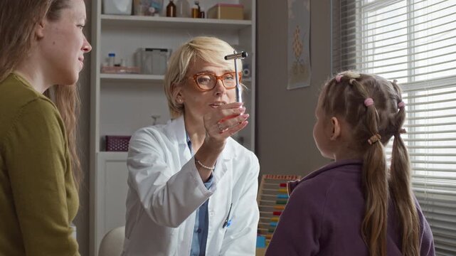 Waist up of Caucasian middle aged female pediatrician testing child eye reflexes with neurological hammer during medical checkup. Footage ideal for pediatric clinic marketing and healthcare services