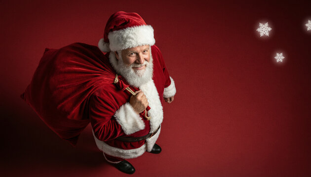 Santa claus carrying a large red sack of gifts over his shoulder, looking up at the camera, isolated on a red background with snowflakes