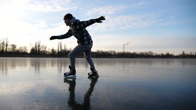 Sportsman skating on frozen river at sunset time. Young man shod in figure skates sliding on ice rink outdoor. Active leisure in cold weather at wintertime. Concept of healthy lifestyle. Slow motion