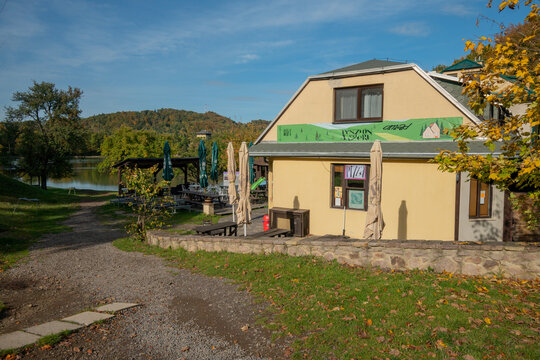 View of the yellow building of a pension near Pocuvadlo Lake with autumn trees and hills under a blue sky in Banska Stiavnica, Banskobystricky kraj, Slovakia.