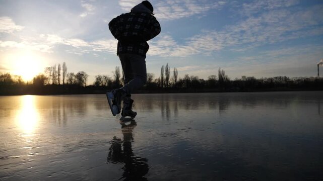 Sportsman skating on frozen river at sunset time. Young man shod in figure skates sliding on ice rink outdoor. Active leisure in cold weather at wintertime. Concept of healthy lifestyle. Slow motion
