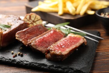 Fototapeta premium Cut tasty beef steak with spices and rosemary on wooden table, closeup