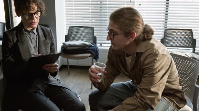 Caucasian female psychotherapist talking to Caucasian teenage boy drinking water during therapy session. Footage for mental health awareness campaigns and counseling services