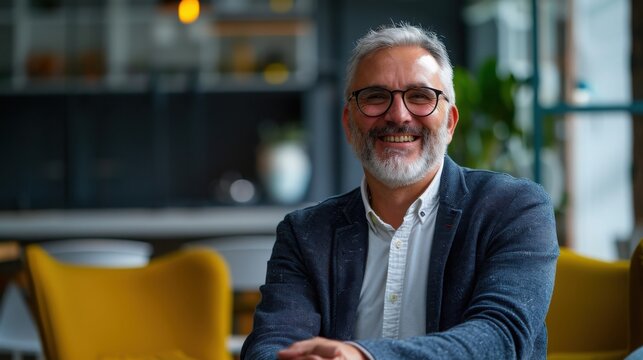 Businessman wearing glasses sits in a modern office lounge while smiling at the camera during a break.