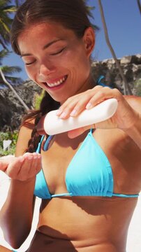 Beach bikini body woman applying sunscreen lotion on shoulder skin relaxing on Caribbean vacation getaway. Mixed race Asian girl putting sun cream - skincare solar protection. Vertical video.