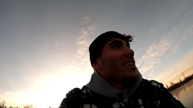Happy male skater sliding on ice rink during beautiful sunset. Young sportsman skating on frozen river at winter day. Guy enjoying sport and having active leisure in cold weather at wintertime. POV