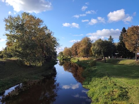 Beautiful autumn landscape with a calm river reflecting a blue sky with white clouds and trees on the banks