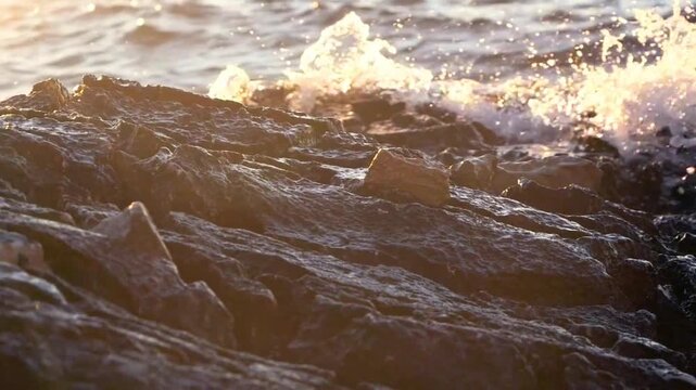 Close-up of powerful water splashing over a wet rocky shoreline during a scenic sunset