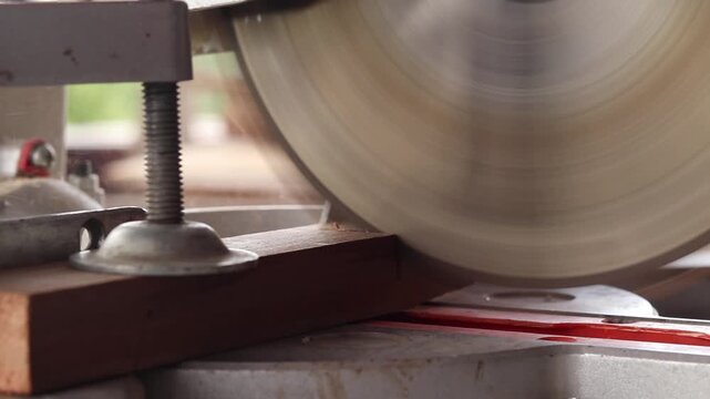 The process of sawing a wooden block with a miter saw. Close-up of the blade in operation. Working with wood, a miter saw cuts a wooden workpiece. The concept of construction and carpentry. Work