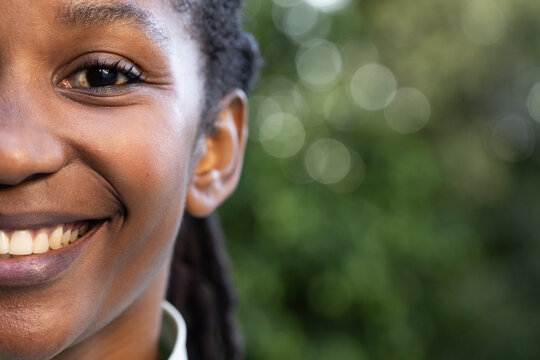 Woman smiling and facing camera on left outdoors with bokeh foliage and shirt collar visible