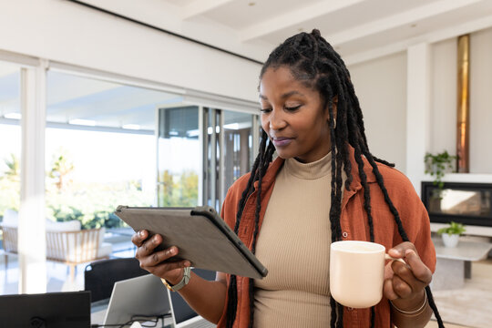Woman standing in modern open-plan home holding tablet and ceramic mug, wearing beige turtleneck