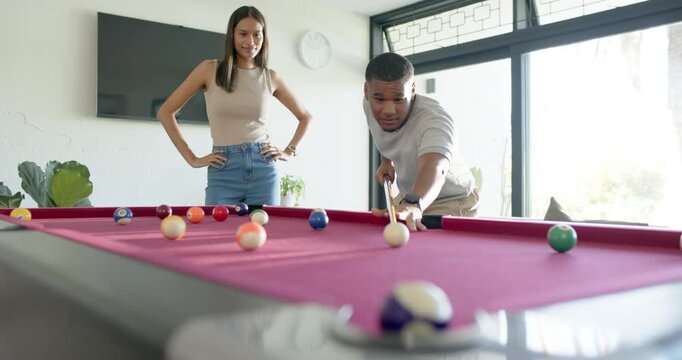 Couple playing pool at home, African American man lining up and striking cue ball taking turn
