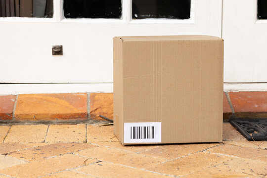 Cardboard delivery box is sitting on terracotta tiles in front of white door, barcode visible
