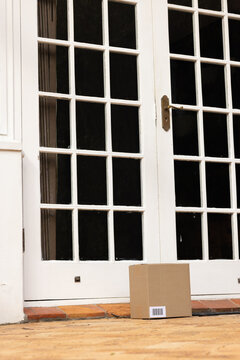 Cardboard delivery box sitting on tiled threshold at white French doors, brass handle visible