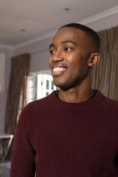 Man standing and smiling while looking right in living room wearing maroon sweater near window