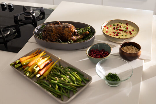 Roasted chicken is resting on gray platter atop quartz countertop, with green beans and dip