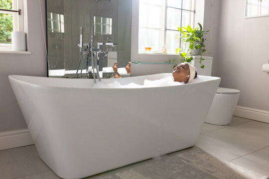 White freestanding bathtub holding bubbles near windows, chrome filler reflected in mirror