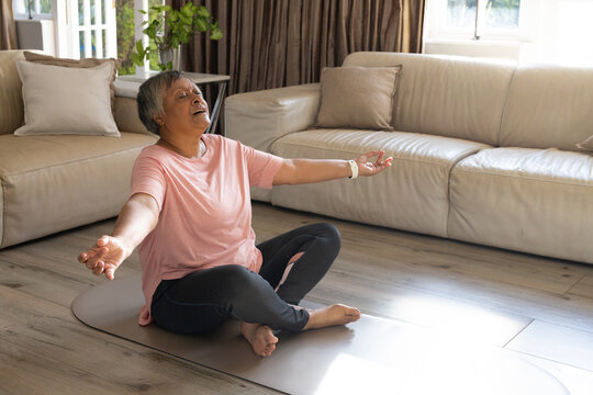 Senior African American woman meditating on gray mat at home, wearing pink tee and smartwatch