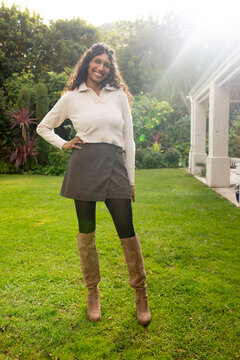 African American woman smiling and posing on backyard lawn with knit sweater and knee-high boots