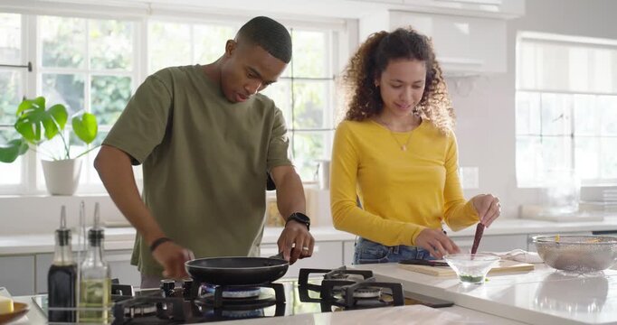 Couple cooking at kitchen island after burner lighting, man adjusting pan while woman prepping meal