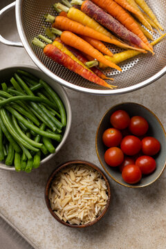 Rainbow carrots are sitting in colander on light counter with green beans, cherry tomatoes, almonds