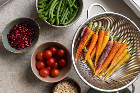 Steel colander holding colorful baby carrots with cherry tomatoes and almonds on counter by window