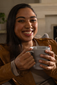 African American woman smiling while holding ribbed mug on couch wearing tan jacket