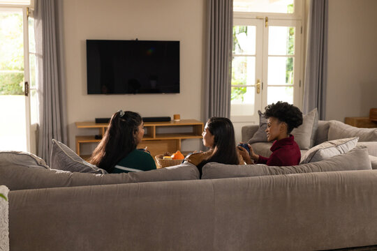 Diverse female friends gathering on gray sectional sofa in home with pumpkin basket on coffee table