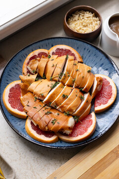 Sliced glazed poultry breast resting on blue plate on counter by window with grapefruit and thyme