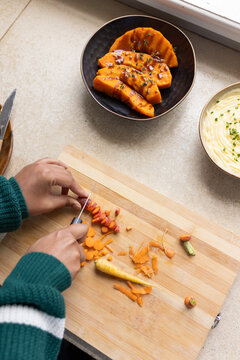Indian woman slicing carrots on wood cutting board in kitchen holding paring knife in green sweater