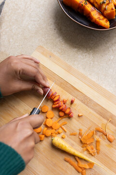 Indian woman slicing purple and orange carrots on wooden board at counter using small knife