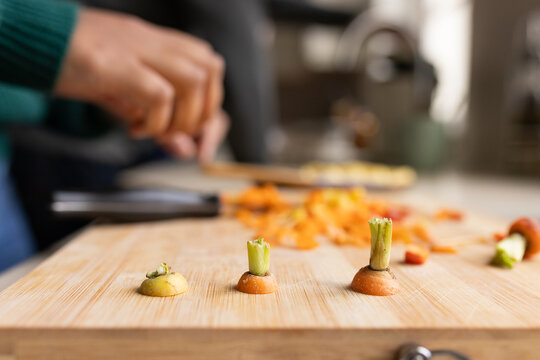 Indian woman in green sweater chopping carrot stubs with green tops on kitchen cutting board