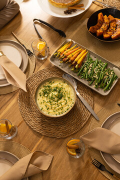 Bowl of mashed potatoes sitting centered on wood table with carrots, green beans, squash, citrus