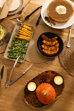 Pumpkin pie is sitting on stand with roasted squash, green beans, lit candles on wooden table