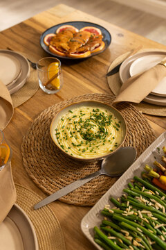 Bowl of mashed potatoes is sitting on wooden dining table, with green beans and carrots