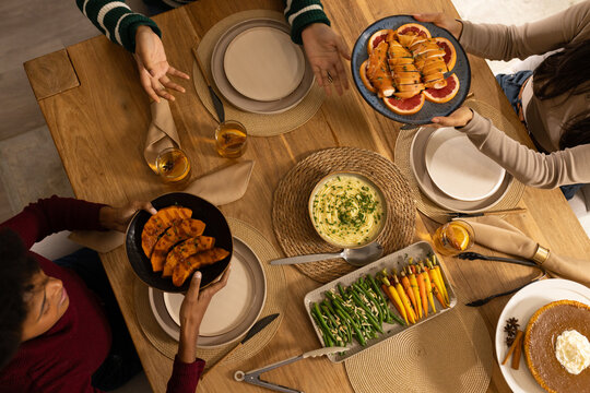 Diverse female friends passing plates and serving roasted squash and poultry at home dining table