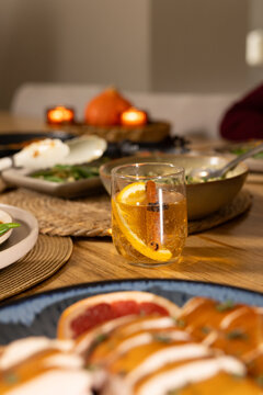 Double-walled glass tumbler is holding amber drink with orange slice and cinnamon stick on table