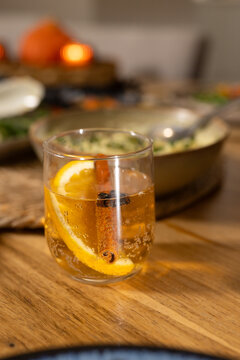 Glass tumbler is holding fizzy amber drink with orange slice and cinnamon stick on wooden table