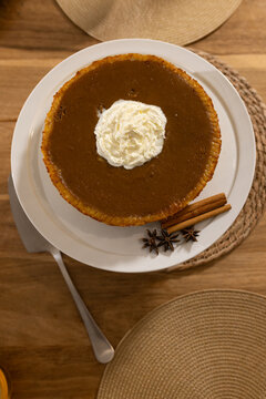 Round spiced pie is sitting on white pedestal plate on wooden table, with whipped cream