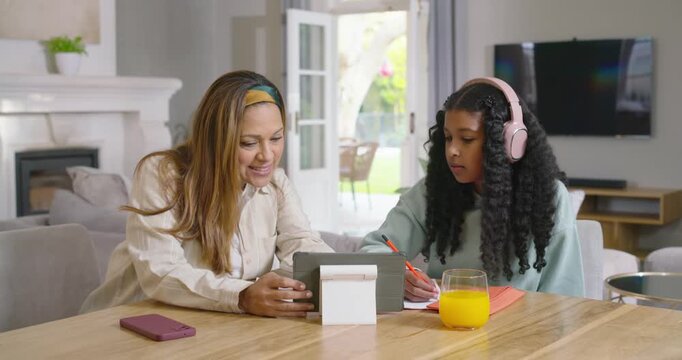 African American mom and teen daughter studying at home, mom pointing tablet lesson as teen writing
