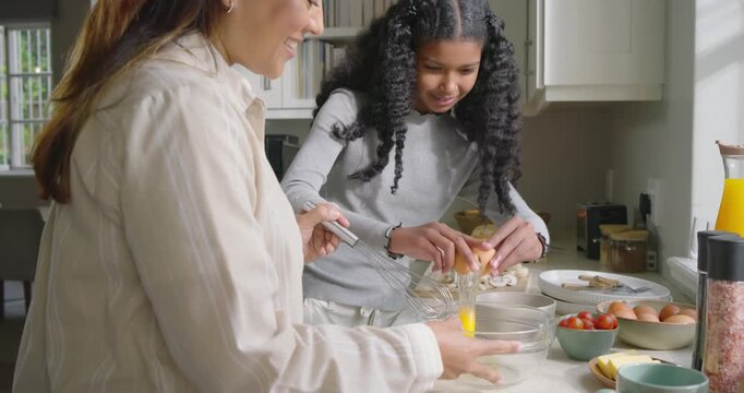 African American mother and daughter at home counter starting breakfast, whisking and cracking eggs