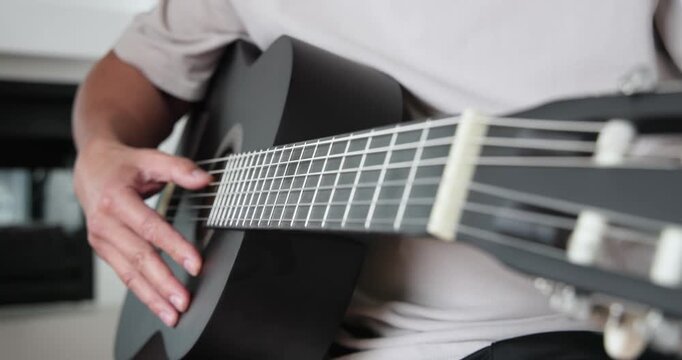 Senior Chinese male plucking strings checking tuning adjusting pegs and playing black guitar on bed