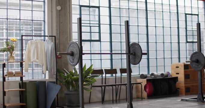 Camera is panning right and down, showing loaded barbell on squat rack, platform, storage, windows