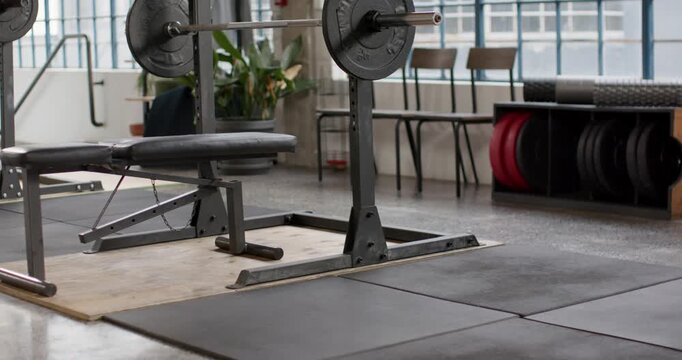 Camera is pulling back and tilting up from low view, revealing loaded barbell and bench centered