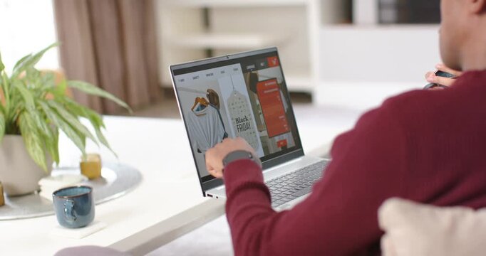 African man shopping on laptop from sofa, holding credit card because Black Friday sale