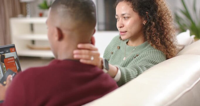 Diverse couple woman leaning on couch, placing hand on man's neck to attract attention at laptop