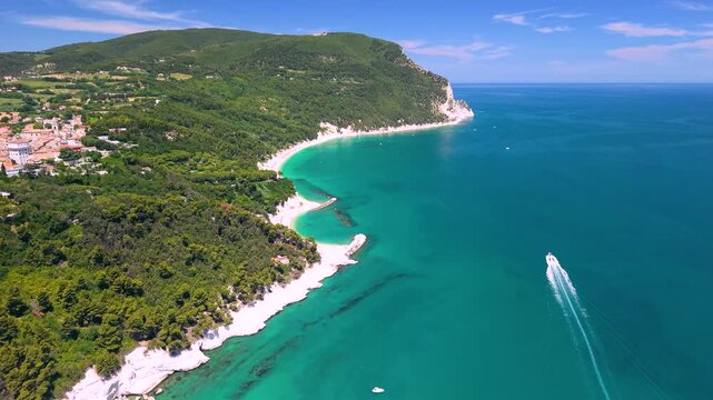 Sirolo Conero Italy 4K Aerial. Drone sideway view of speedboat racing in turquoise Adriatic sea revealing historic hilltop perched village on white cliffs landscape. Marche luxury travel asset